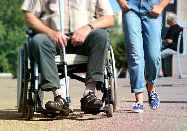 man on a wheelchair being wheeled over resin gravel by two helpers