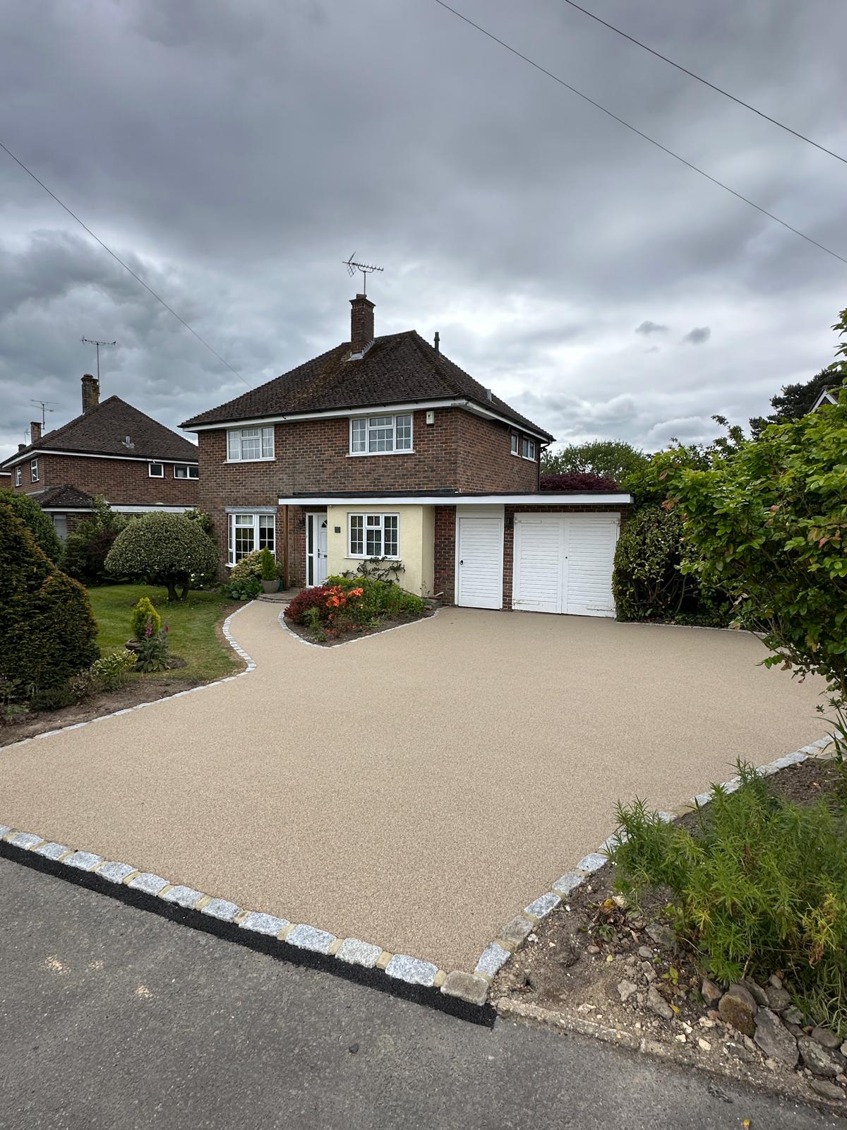 Two-story brick house with a beige front entry, attached double garage, and well-kept front garden on a gravel driveway under a cloudy sky